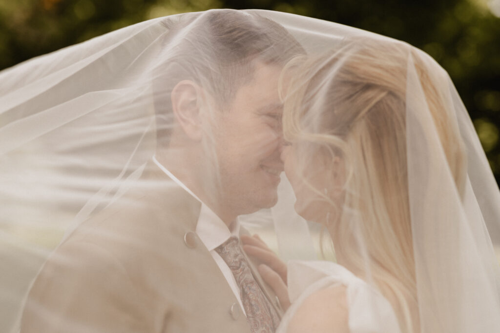 Brautpaar unter einem Schleier am lachen und küssen, Hochzeitsplanung Deutschland, Lunaris Event Planning