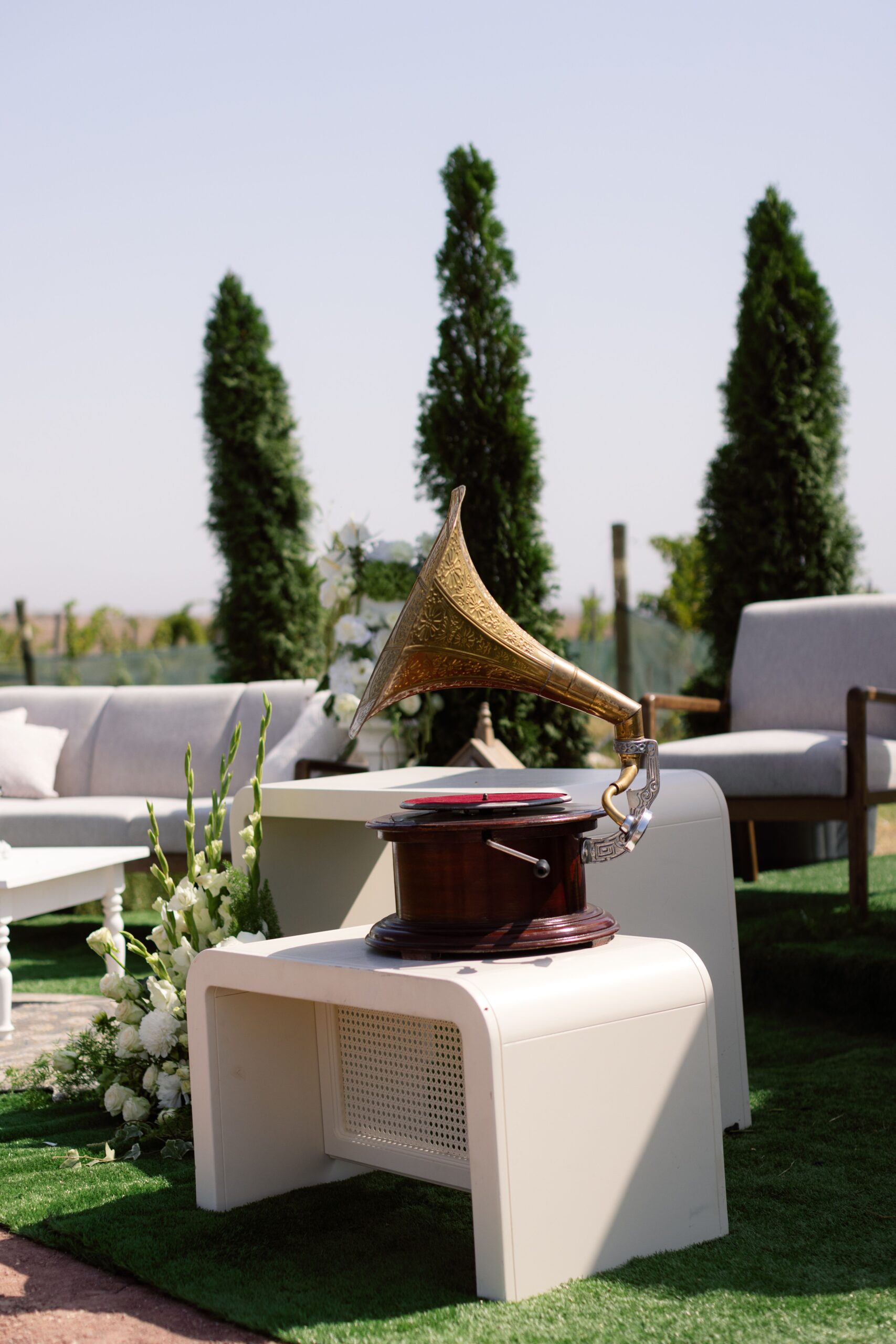 An elegant outdoor vintage setup with a gramophone, white chairs, and floral arrangements